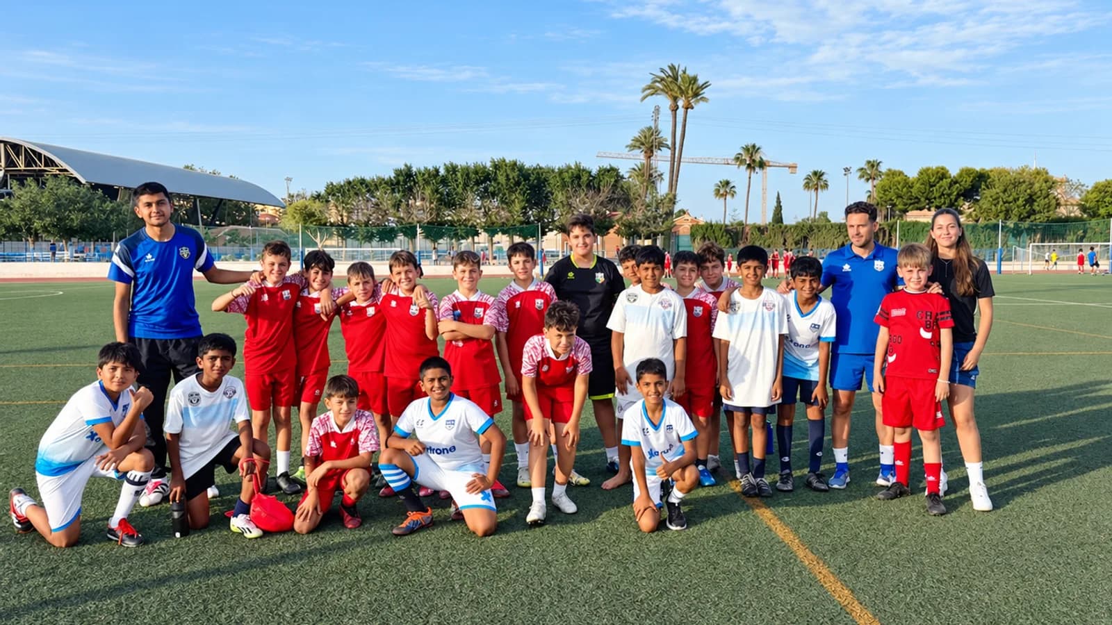 A squad of young footballers and their coaches together on a Spanish academy pitch at golden hour.